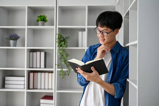 Jonge student die met glazen een leerboek in de studeerkamer leest