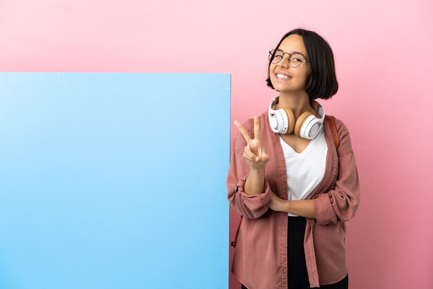 Jonge student gemengd ras vrouw met een grote banner over geïsoleerde achtergrond glimlachend en overwinningsteken tonen