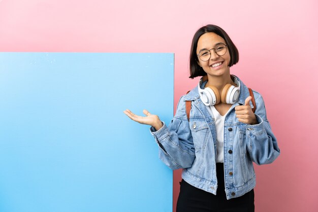 Jonge student gemengd ras vrouw met een grote banner over geïsoleerde achtergrond met copyspace denkbeeldig op de palm om een advertentie in te voegen en met duimen omhoog