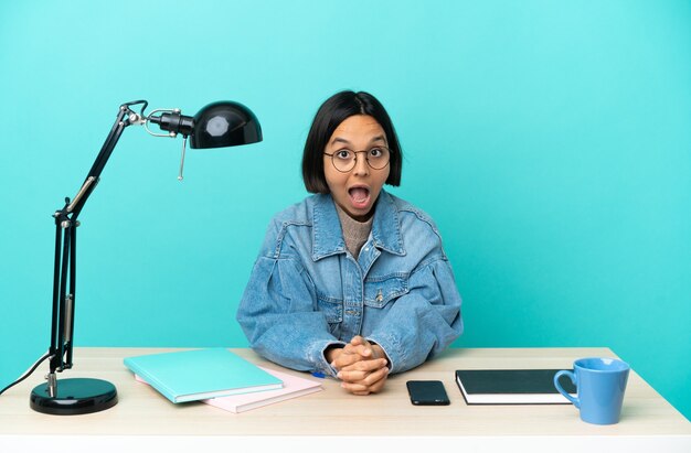 Jonge student gemengd ras vrouw studeert op een tafel met verrassingsgelaatsuitdrukking