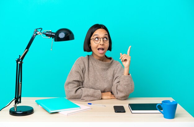 Jonge student gemengd ras vrouw studeren op een tafel die omhoog wijst en verrast