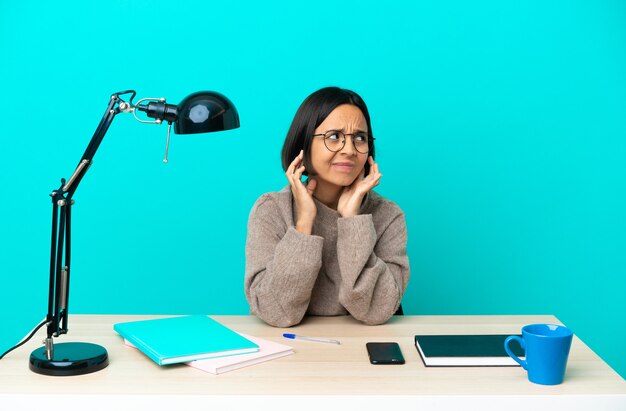 Jonge student gemengd ras vrouw studeren op een tafel gefrustreerd en oren bedekt