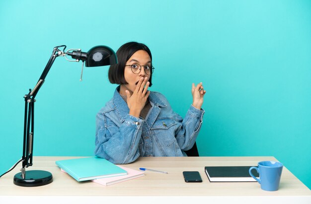 Jonge student gemengd ras vrouw studeren op een tafel met verrassende uitdrukking terwijl ze naar de kant wijst