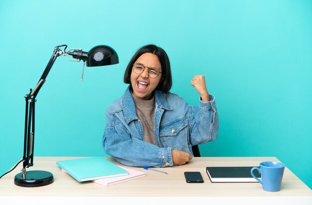 Jonge student gemengd ras vrouw studeren op een tafel vieren een overwinning