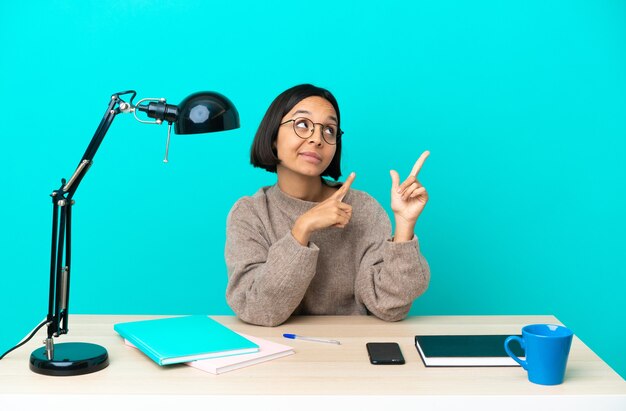 Jonge student gemengd ras vrouw studeren op een tafel wijzend met de wijsvinger een geweldig idee