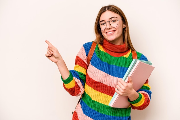 Jonge student kaukasische vrouw geïsoleerd op een witte achtergrond glimlachend en opzij wijzend met iets op lege ruimte