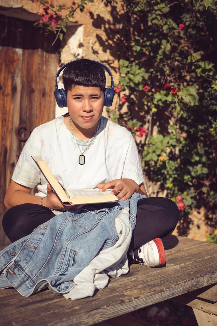Foto jonge student lezen en luisteren naar muziek zittend in de tuin