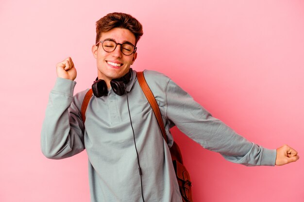 Jonge student man geïsoleerd op roze muur dansen en plezier maken.