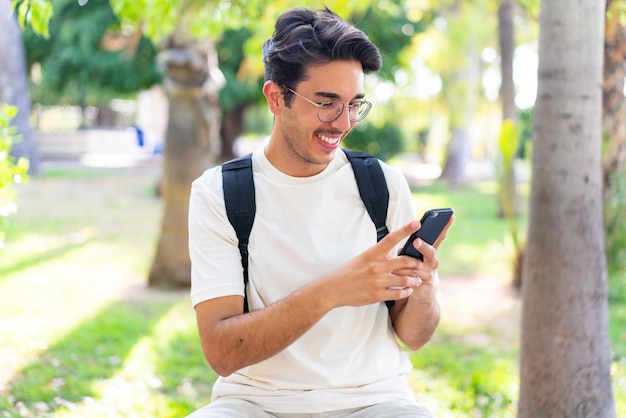 Jonge student man in de buitenlucht met behulp van mobiele telefoon