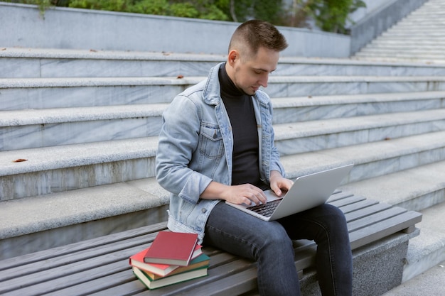 Jonge student man zit met laptop Blanke man werkt of studeert met notebook buitenshuis