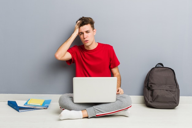 Jonge student man zittend op zijn huisvloer met een laptop