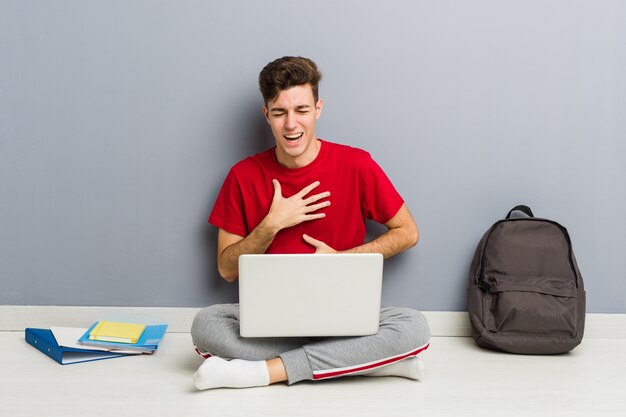 Jonge student man zittend op zijn huisvloer met een laptop