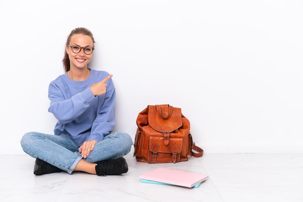 Jonge student meisje zittend op de vloer geïsoleerd op een witte achtergrond wijzend naar achteren