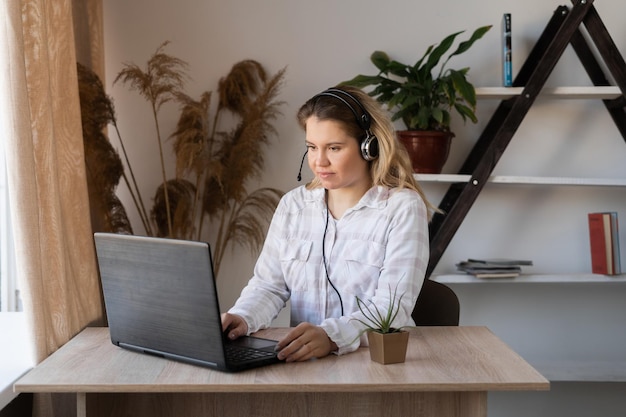 Jonge student met behulp van laptop zittend aan café tafel blonde vrouwelijke student met behulp van draagbare laptopcomputer tijdens het werk aan de cursussen Meisje kijken naar film online op draagbare pc en elektronische oortelefoons