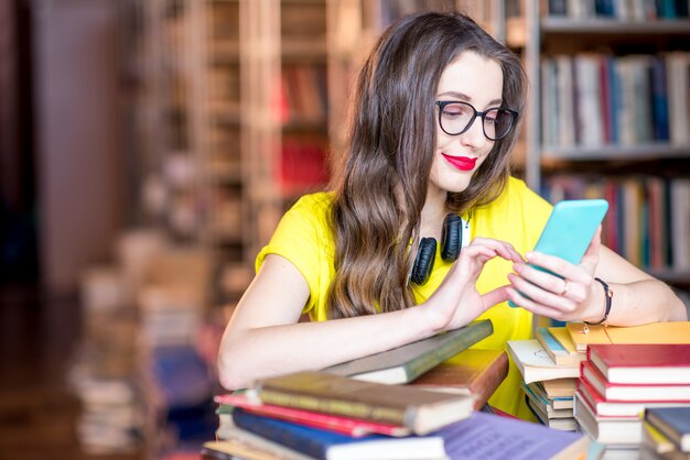 Jonge student met behulp van slimme telefoon in de bibliotheek