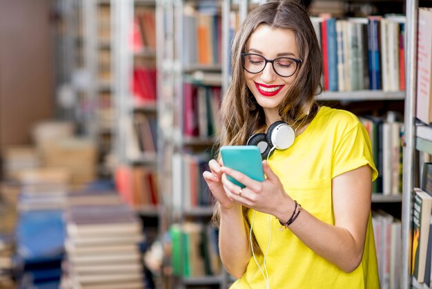 Jonge student met behulp van slimme telefoon in de bibliotheek