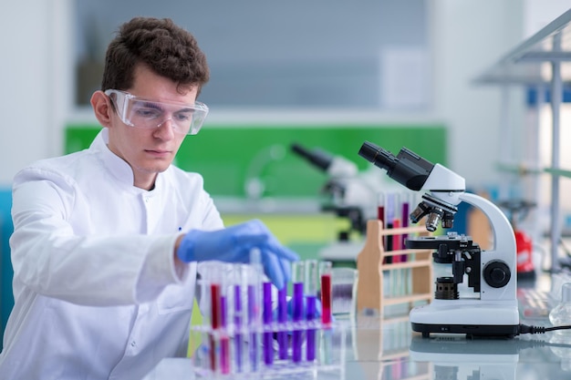 jonge student met een beschermende bril die een scheikunde-experiment maakt in een helder laboratorium-, onderwijs- en medicijnconcept