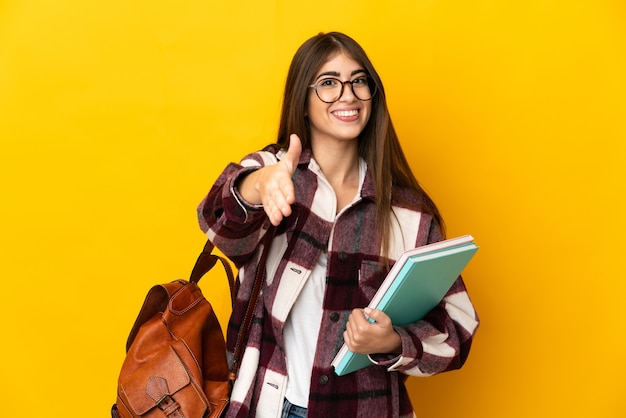 Jonge student vrouw geïsoleerd op gele achtergrond handen schudden voor het sluiten van een goede deal