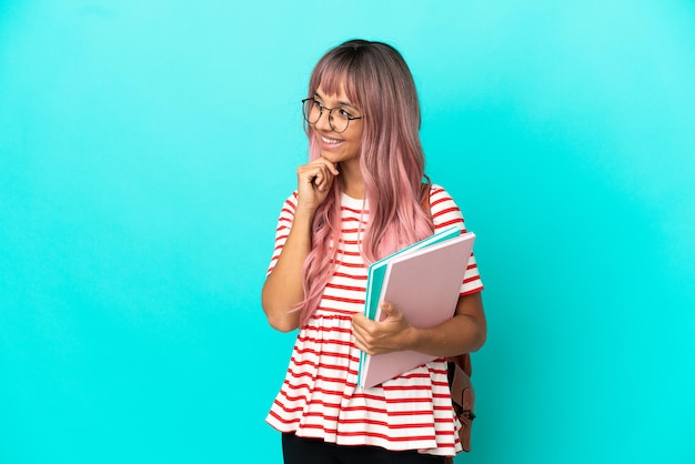 Jonge student vrouw met roze haar geïsoleerd op een blauwe achtergrond terwijl ze glimlacht