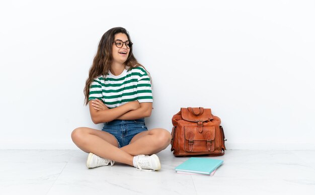 Jonge student vrouw zittend op de vloer geïsoleerd op een witte achtergrond gelukkig en lachend