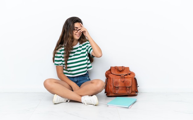 Jonge student vrouw zittend op de vloer geïsoleerd op een witte achtergrond lachen