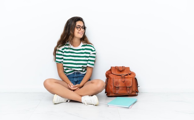 Jonge student vrouw zittend op de vloer geïsoleerd op een witte achtergrond op zoek naar kant