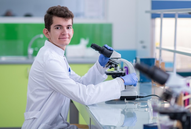 Jonge student-wetenschapper die door een microscoop kijkt terwijl hij wat onderzoek doet in het laboratorium