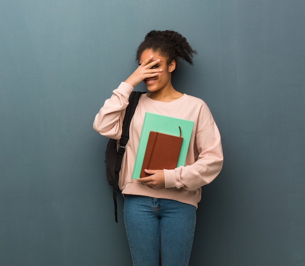 Jonge student zwarte vrouw in verlegenheid gebracht en tegelijkertijd lachen. ze houdt boeken vast.