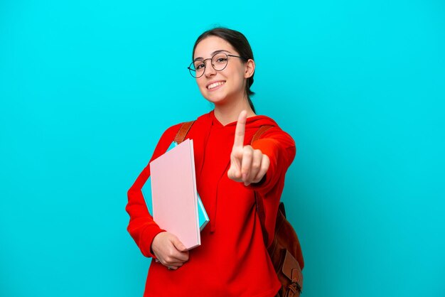 Jonge studente blanke vrouw die op blauwe achtergrond wordt geïsoleerd die een vinger toont en opheft