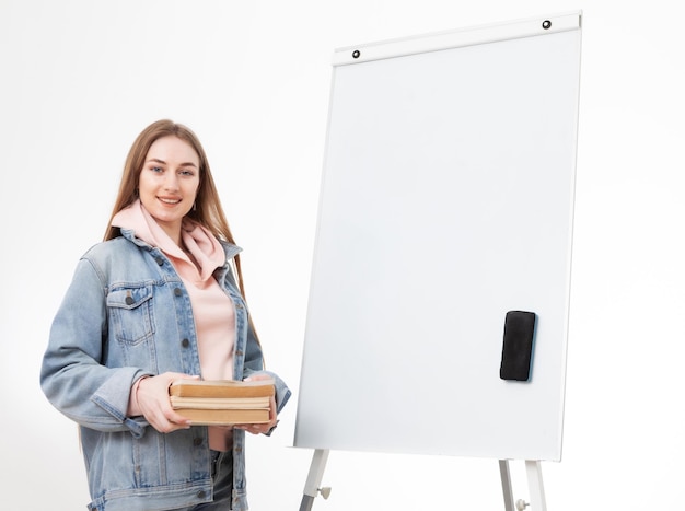 Jonge studente in denim kleding met boeken en wit bord geïsoleerd op witte achtergrond Onderwijs concept