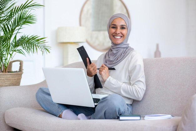 Jonge studente van oosterse afkomst in hijab studeert vanuit huis zittend op de bank in de lotus