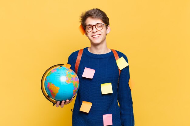 Jonge studentenjongen die gelukkig glimlacht met een hand op de heup en een zelfverzekerde, positieve, trotse en vriendelijke houding