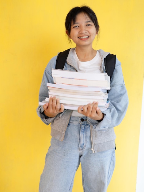 Foto jonge studentenmeisje draagt veel boeken op haar arm met rugzak