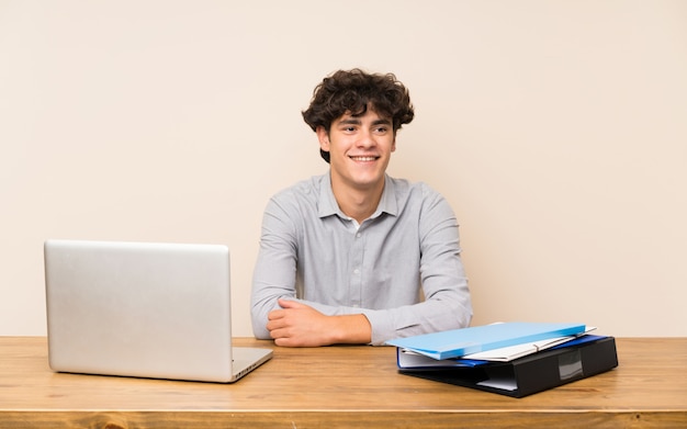 Jonge studentenmens met laptop het stellen met wapens bij heup en het glimlachen