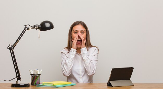 Jonge studentenvrouw die aan haar bureau werken die iets schreeuwen gelukkig aan de voorzijde