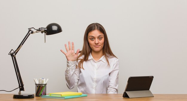 Jonge studentenvrouw die aan haar bureau werkt dat nummer vijf toont