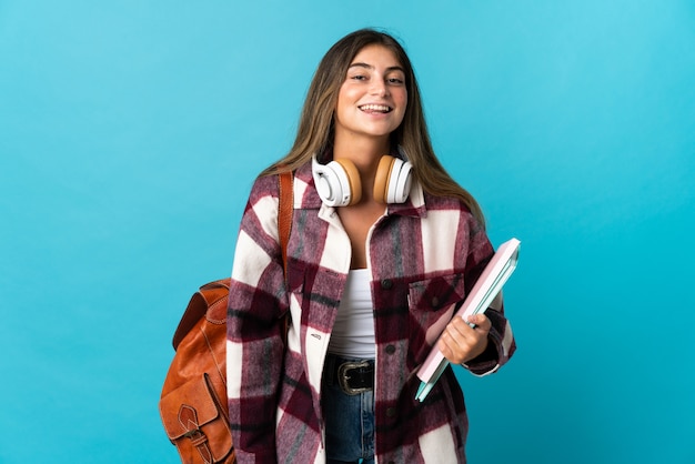 Jonge studentenvrouw die bij het blauwe stellen met wapens bij heup en het glimlachen wordt geïsoleerd