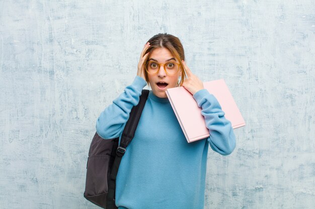 Jonge studentenvrouw die geschokt en geschokt voelen, handen opheffen en in paniek raken bij een fout grunge muur