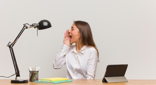 Jonge studentenvrouw die haar bureau werkt die roddel ondertoon fluisteren