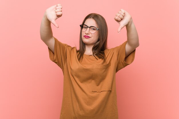 Jonge studentenvrouw die oogglazen dragen die duim tonen en afkeer uitdrukken.