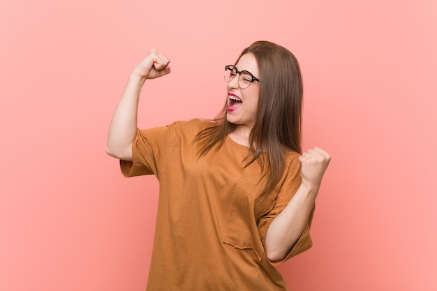 Jonge studentenvrouw die oogglazen dragen die vuist na een overwinning, winnaarconcept opheffen.