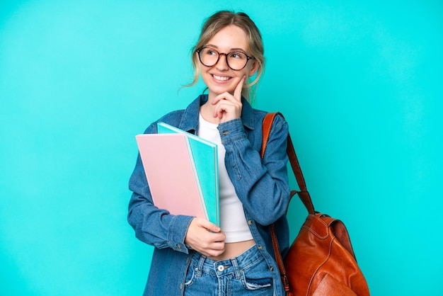 Jonge studentenvrouw die op blauwe achtergrond wordt geïsoleerd die een idee denkt terwijl het kijken