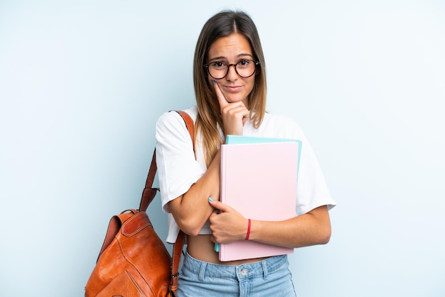 Jonge studentenvrouw die op blauwe achtergrond wordt geïsoleerd die twijfels heeft en denkt