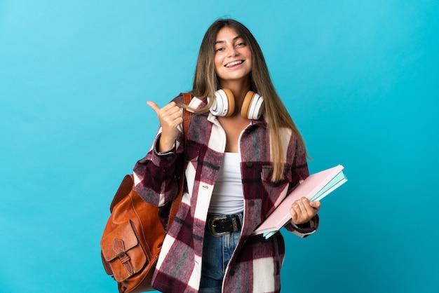 Jonge studentenvrouw die op blauwe muur wordt geïsoleerd die naar de kant wijst om een product te presenteren