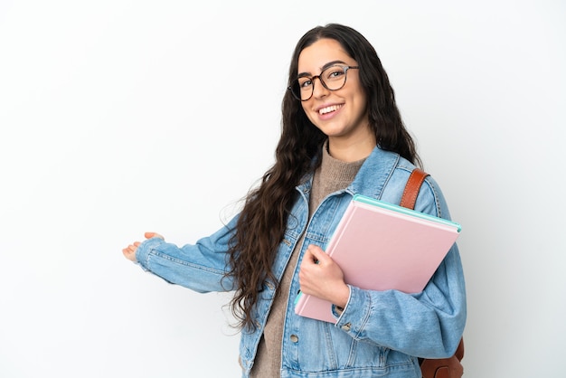 Jonge studentenvrouw die op witte achtergrond wordt geïsoleerd die de handen uitbreidt aan de kant om uit te nodigen om te komen