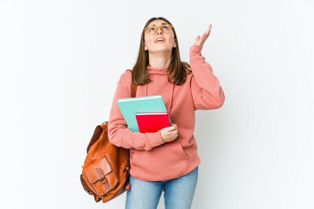 Jonge studentenvrouw die op witte bakcground wordt geïsoleerd die naar de hemel gilt, omhoog kijkt, gefrustreerd.