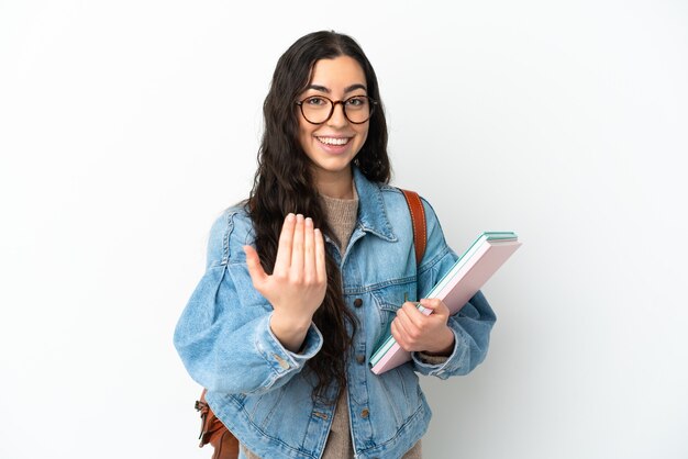 Jonge studentenvrouw die op witte muur wordt geïsoleerd die uitnodigt om met hand te komen. Blij dat je gekomen bent