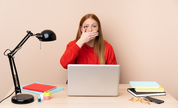 Jonge studentenvrouw in een werkplaats met laptop die mond behandelen met handen