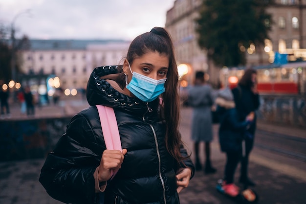 Jonge studentenvrouw met medisch masker buitenshuis met een rugzak