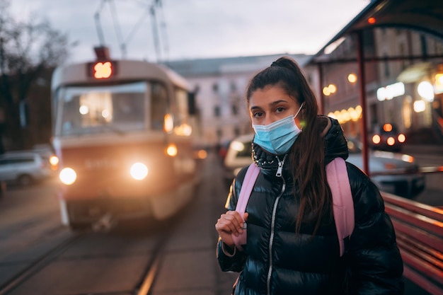 Jonge studentenvrouw met medisch masker buitenshuis met een rugzak